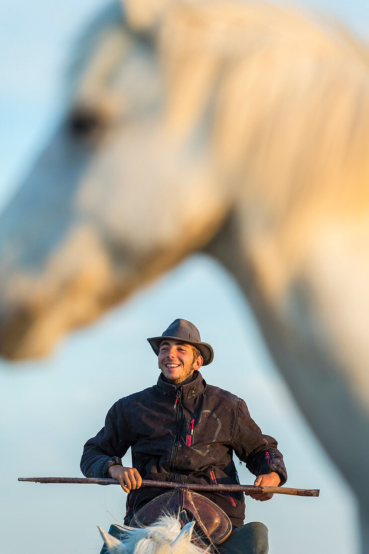 Camargue, France. Cowboy on horseback holding a cattle prod and smiling.