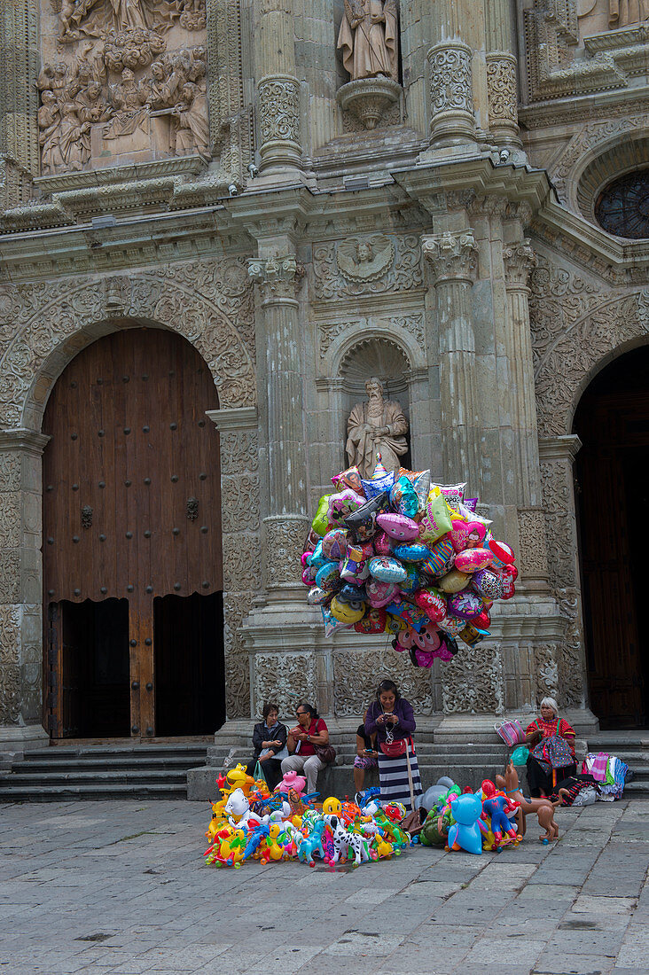 People selling balloons on the square in front of the Cathedral of Our Lady of the Assumption built in a neoclassical style, in the city of Oaxaca de Juarez, Oaxaca, Mexico.
