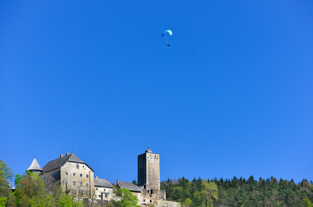 Ein Paraglider schwebt über einer Burg an der Donau bei Wesenufer, Österreich