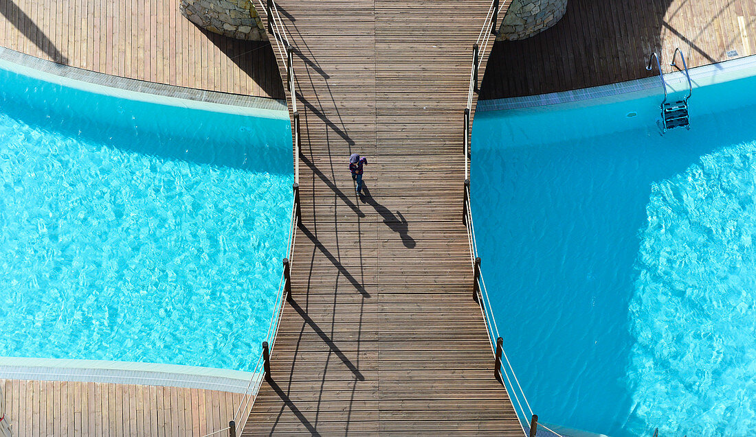 Blick von oben auf einen Jungen, der auf einer Holzbrücke über einen Swimming-Pool geht, Vilamoura, Portugal