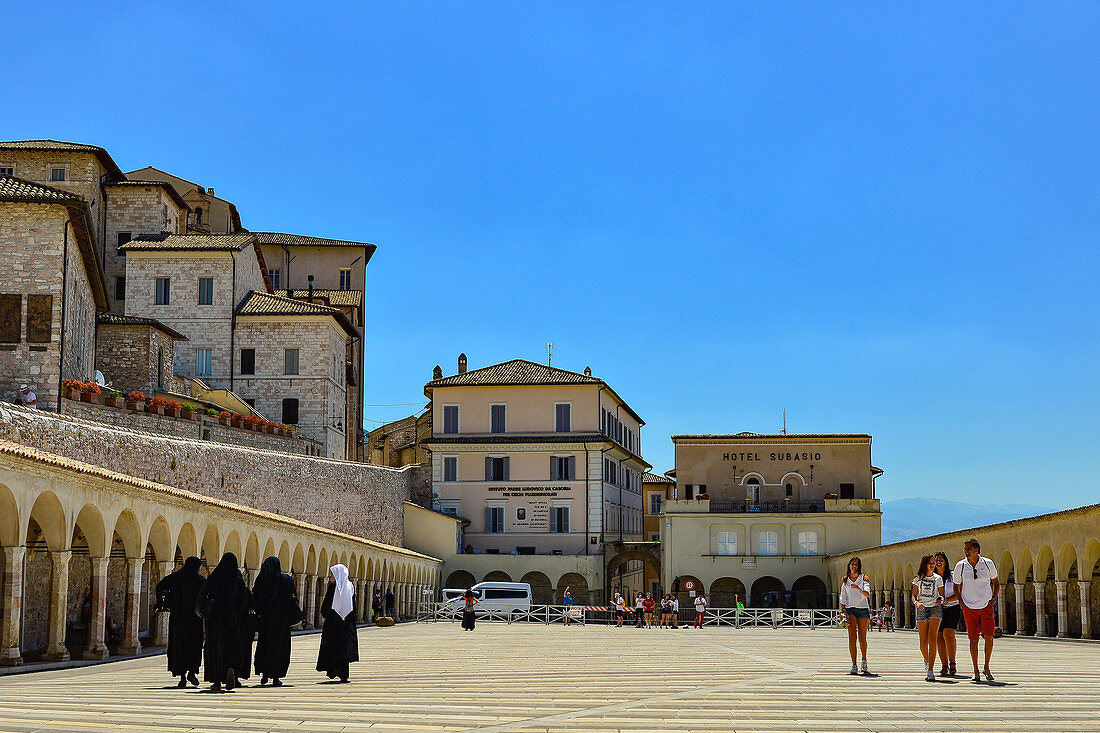 Nonnen und Touristen begegnen sich im Hof der Basilika San Francesco, Assisi, Umbrien, Italien