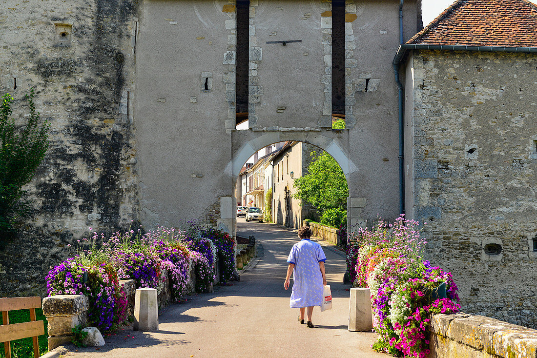 An old woman walks through the city gate decorated with colorful flowers, Liverdun, France