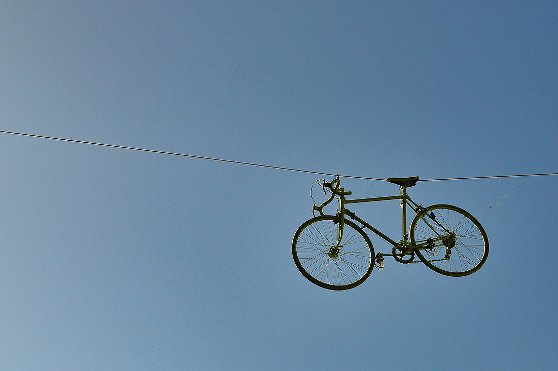 Ein Fahrrad hängt an einem Seil hoch über einer Straße, bei Le Puy, Frankreich