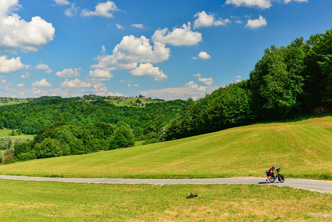 Eine Radfahrerin schiebt das voll bepackte Reiserad eine extrem steile Straße hinauf, bei Rogatec, Slowenien