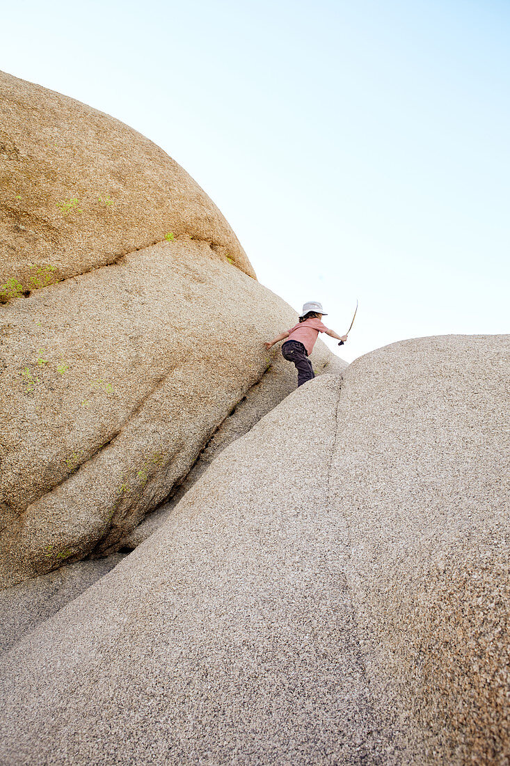 Boy playing on a rock of Jumbo Rocks in Joshua Tree Park, California, USA.