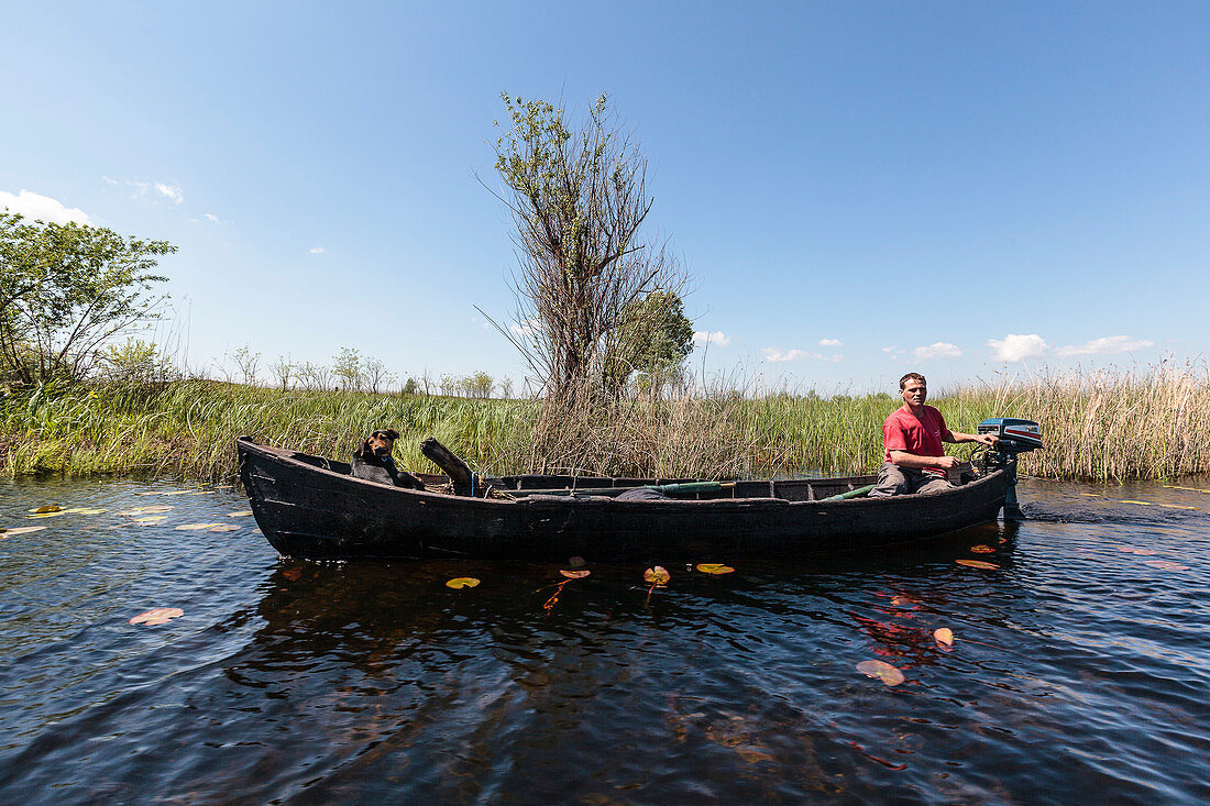 Danube Delta, fisherman and dog in wooden boat, Sulina, Tulcea, Romania.