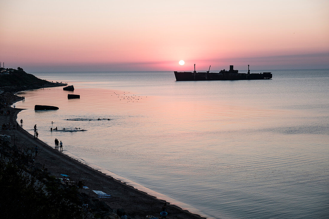 Das Schiffswrack Evangelia, Menschen und Möwen bei Sonnenaufgang an der Schwarzmeerküste in Costinesti, Constanta, Rumänien.