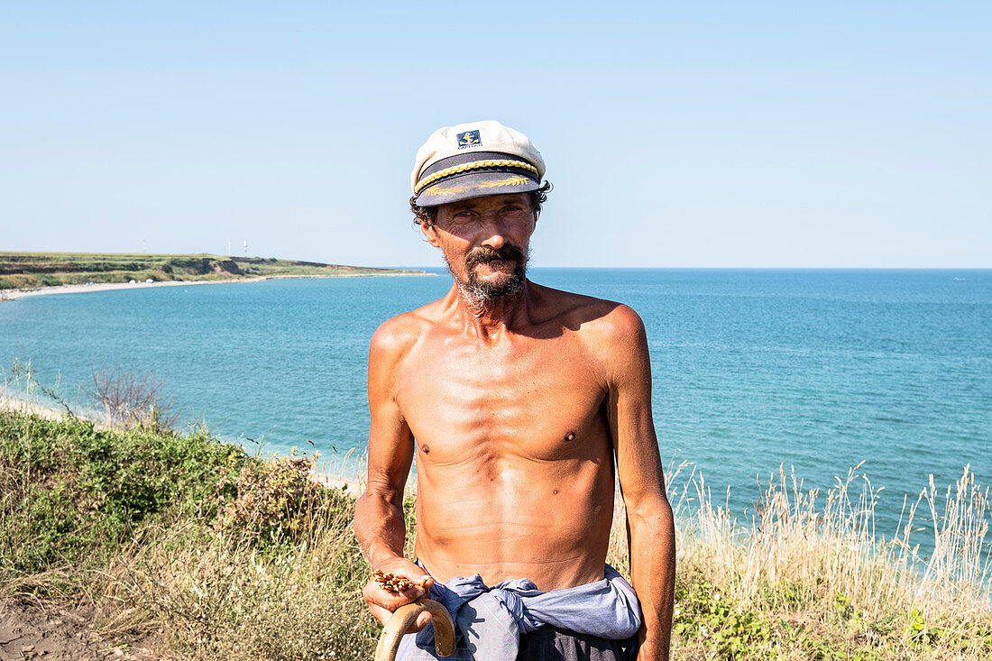 Shepherd with a shirtless captain's hat, Black Sea coast, holding pretzel sticks in his hand, Costinesti, Constanta, Romania.