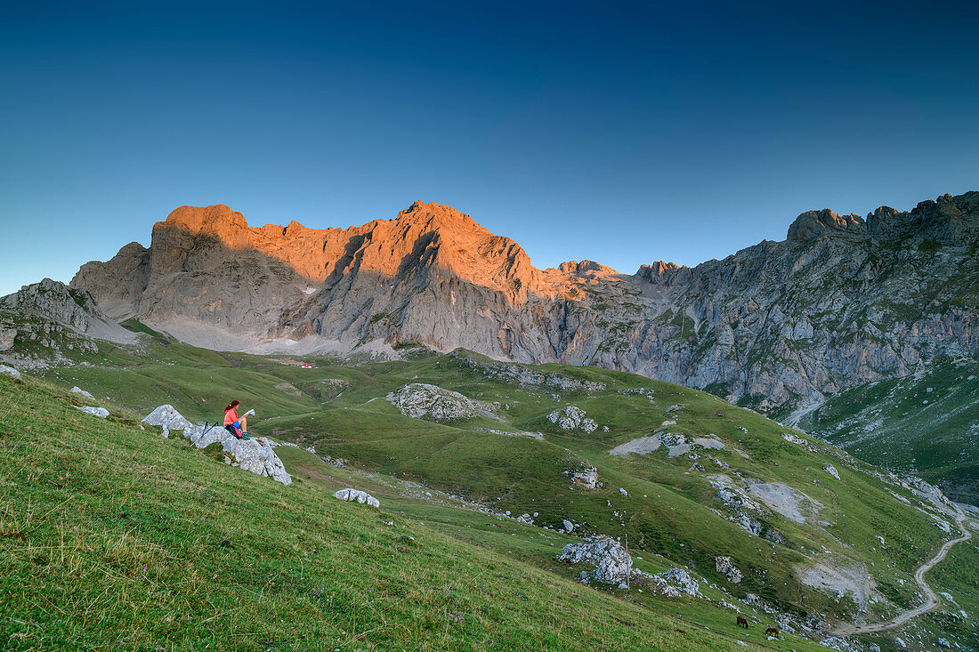 Hiking woman sitting on rock and looking at map, Pena Vieya in the morning light in the background, Pena Vieja, Picos de Europa, Picos de Europa National Park, Cantabrian Mountains, Cantabria, Spain