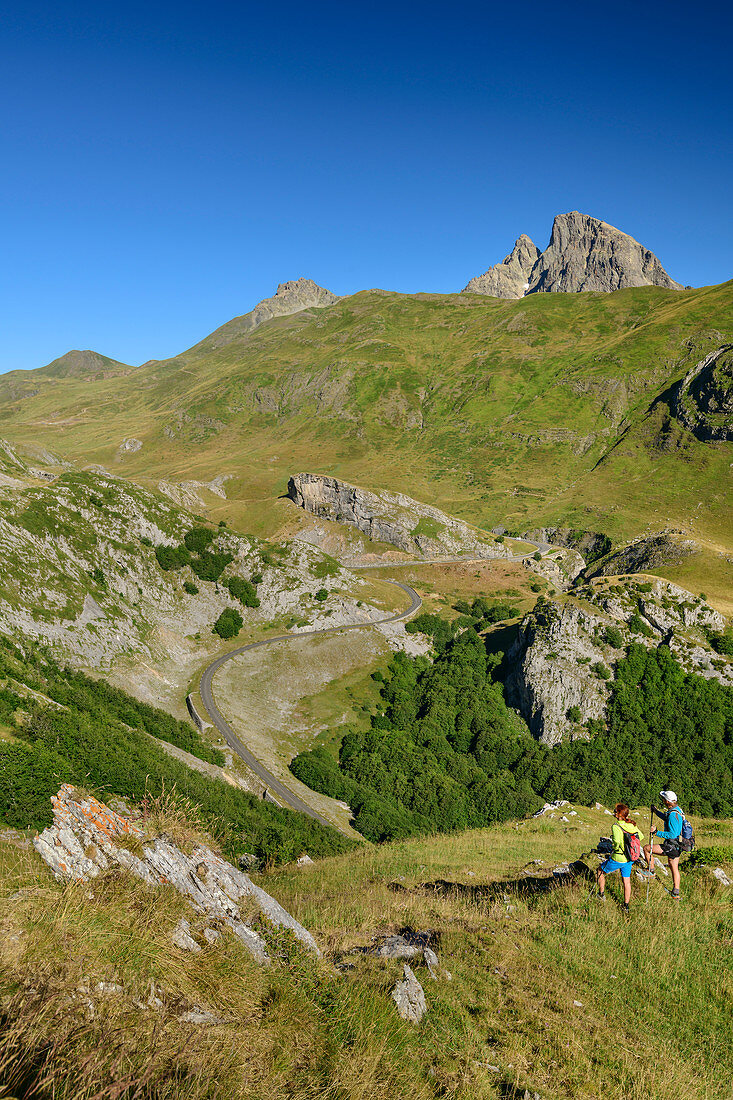 Mann und Frau beim Wandern blicken auf Passstraße Col du Pourtalet, Pic du Midi d´Ossau im Hintergrund, Col du Pourtalet, Nationalpark Pyrenäen, Pyrénées-Atlantiques, Pyrenäen, Frankreich