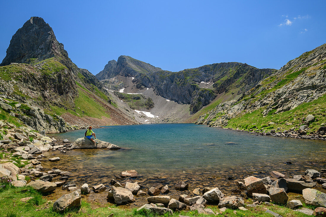 Woman while hiking sits on rock island, Lac d´Arious, Pyrenees National Park, Pyrénées-Atlantiques, Pyrenees, France