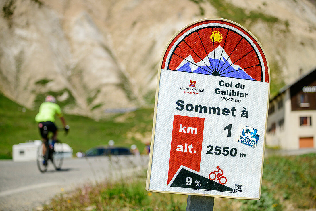 Information board for cyclists at Col du Galibier with cyclists out of focus in the background, Col du Galibier, Hautes-Alpes, Savoie, France