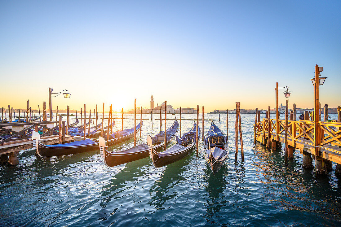 Gondeln nahe Markusplatz mit San Giorgio-Insel auf dem Hintergrund während des Sonnenaufgangs. Venedig, Venetien, Italien.
