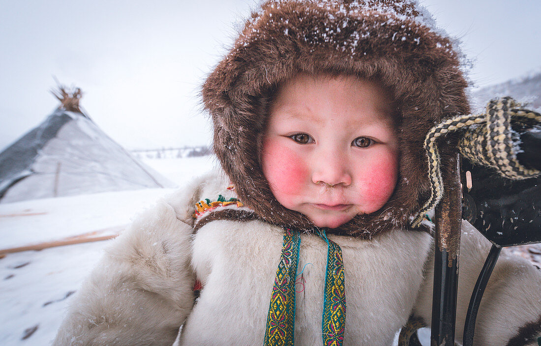 Ein junger Nenzenjunge, gekleidet mit dem traditionellen Mantel. Alltag im Lager der nomadischen Rentierhirten. Polar Ural, Yamalo-Nenets autonomer Okrug, Sibirien, Russland