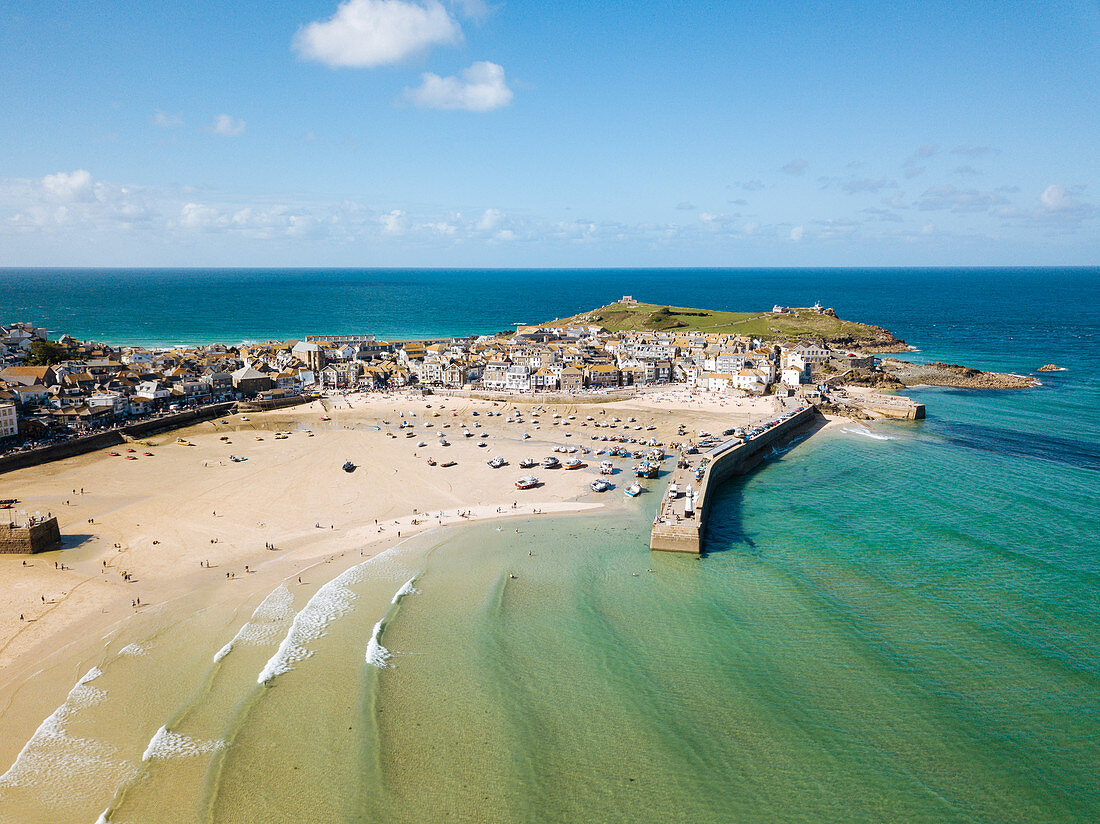 Aerial View of St Ives, a wide sandy beach and sheltered harbour with boats beach on sand at low tide.