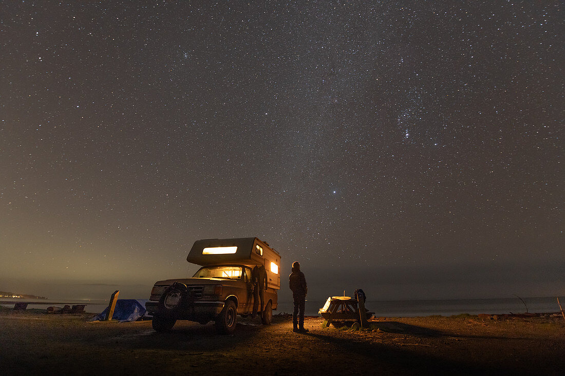 Person standing next to camper-van parked near Jordan River, British Columbia, Canada at night.
