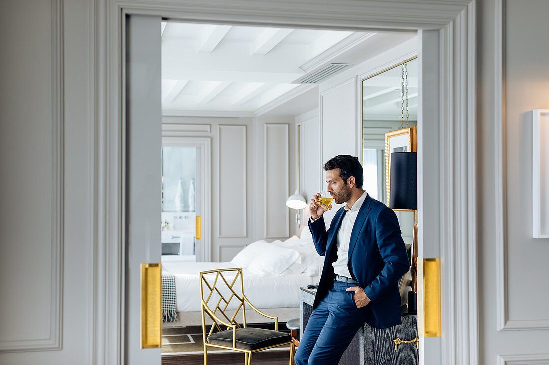 Businessman with iced drink, deep in thoughts in suite