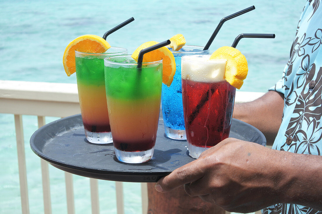 Pacific islander male waiter serving cocktails on a tropical pacific island resort in Rarotonga, Cook Islands. Drinks background. Copy space