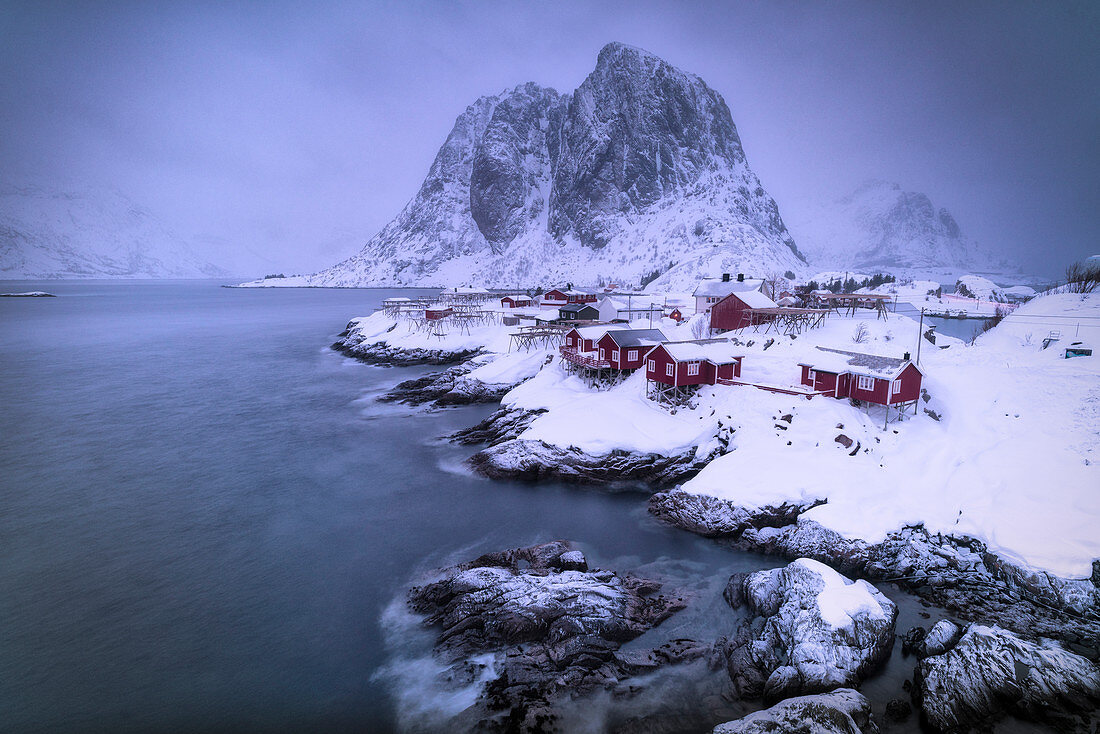 Dämmerung über dem eisigen Meer, das das mit Schnee bedeckte Fischerdorf Hamnoy, Nordland, Lofoten-Inseln, Norwegen umgibt
