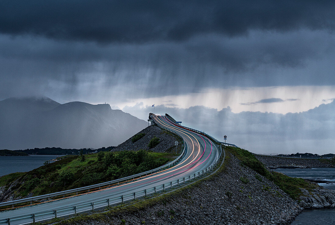 Gewitterwolken über Autolichtspuren auf Storseisundet Brücke, Atlantikstraße, mehr og Romsdal Grafschaft, Norwegen