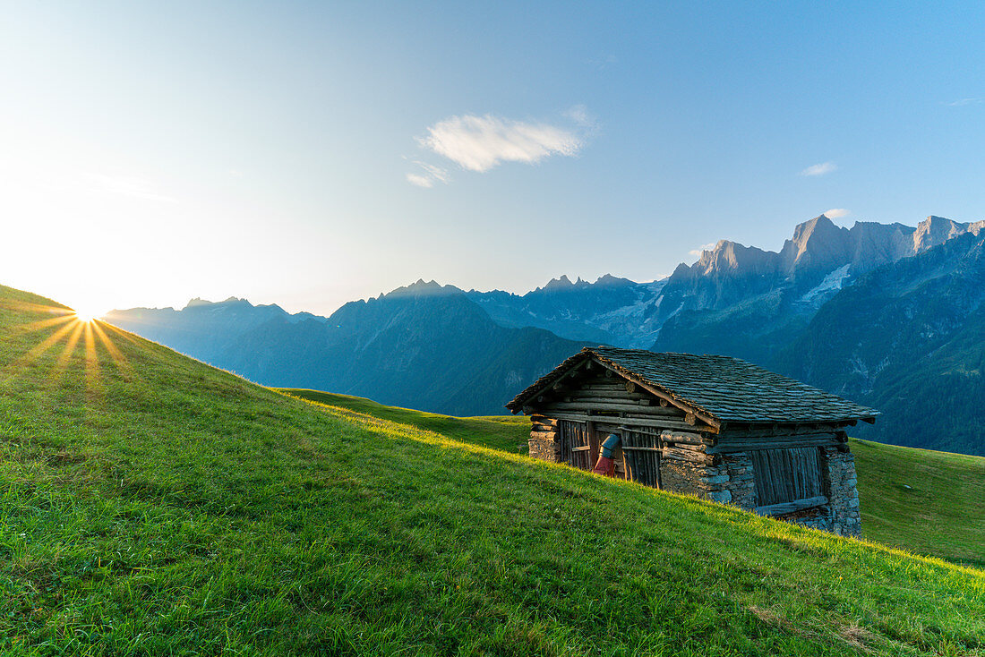 Sunburst über den grünen Wiesen der Tombal Alp, Soglio, Val Bregaglia, Kanton Graubunden, Schweiz