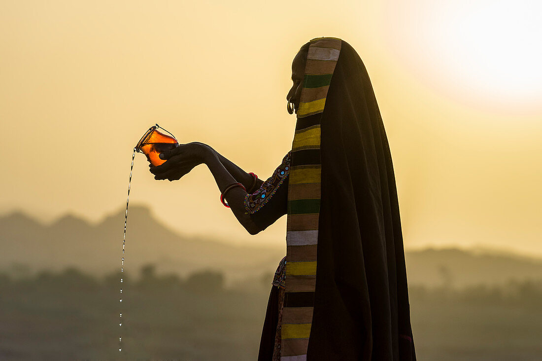 Ahir Frau im traditionellen bunten Stoff, der Wasser bei Sonnenuntergang, Great Rann von Kutch Desert, Gujarat, Indien, Asien gießt