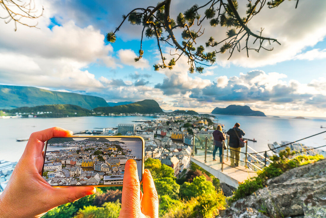 Hands holding smartphone photographing Alesund from Byrampen viewpoint, More og Romsdal county, Norway, Scandinavia, Europe