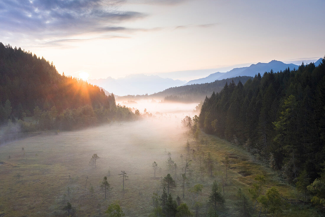 Sonnenstrahlen bei Sonnenaufgang auf Nebel, der das Feuchtgebiet des Reservats Pian di Gembro, Luftaufnahme, Aprica, Valtellina, Lombardei, Italien, Europa bedeckt