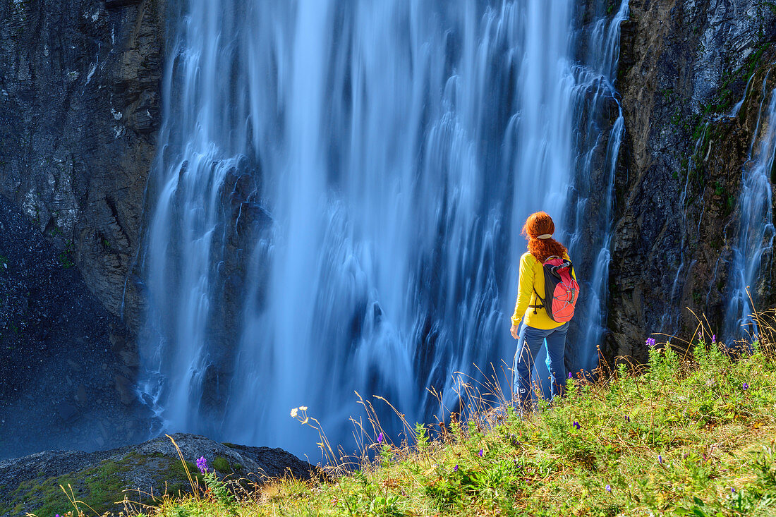 Woman hiking stands in meadow and looks at waterfall, Engstligenfall, Adelboden, Bernese Alps, Bern, Switzerland