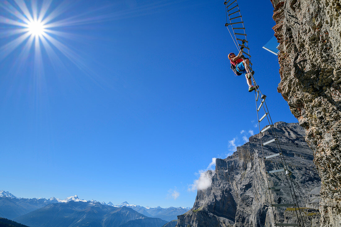 Woman climbs on overhanging ladder on adventure via ferrata Gemmi, Valais Alps in the background, Gemmi, Bernese Alps, Valais, Switzerland