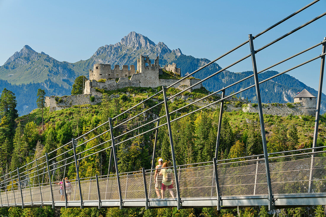 Mehrere Personen gehen über die Seilbrücke Highline 179 mit Burgruine Ehrenberg im Hintergrund, Reutte, Tirol, Österreich