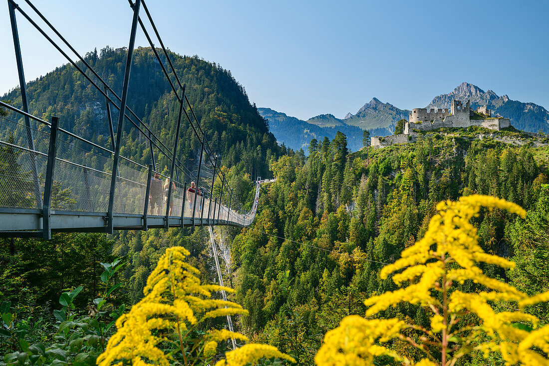 Several people walk over the Highline 179 rope bridge with Ehrenberg castle ruins in the background, Reutte, Tyrol, Austria