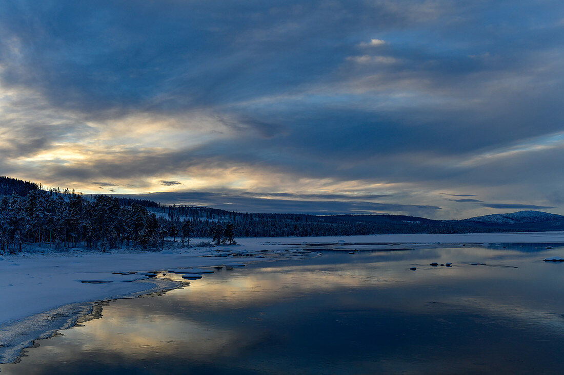 Winterstimmung mit leuchtenden Wolken an einem See in Lappland, Arjeplog, Schweden