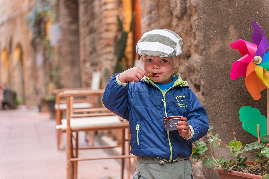 A young boy enjoys his chocolate ice cream in the alleys of San Gimignano, Province of Siena, Tuscany, Italy
