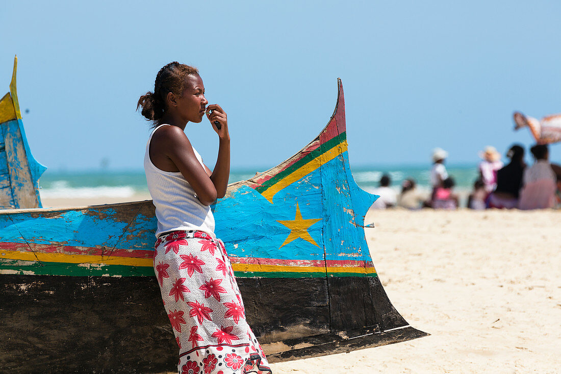 Junge Frau lehnt an Fischerboot am Strand bei Morondava, Madagaskar, Afrika