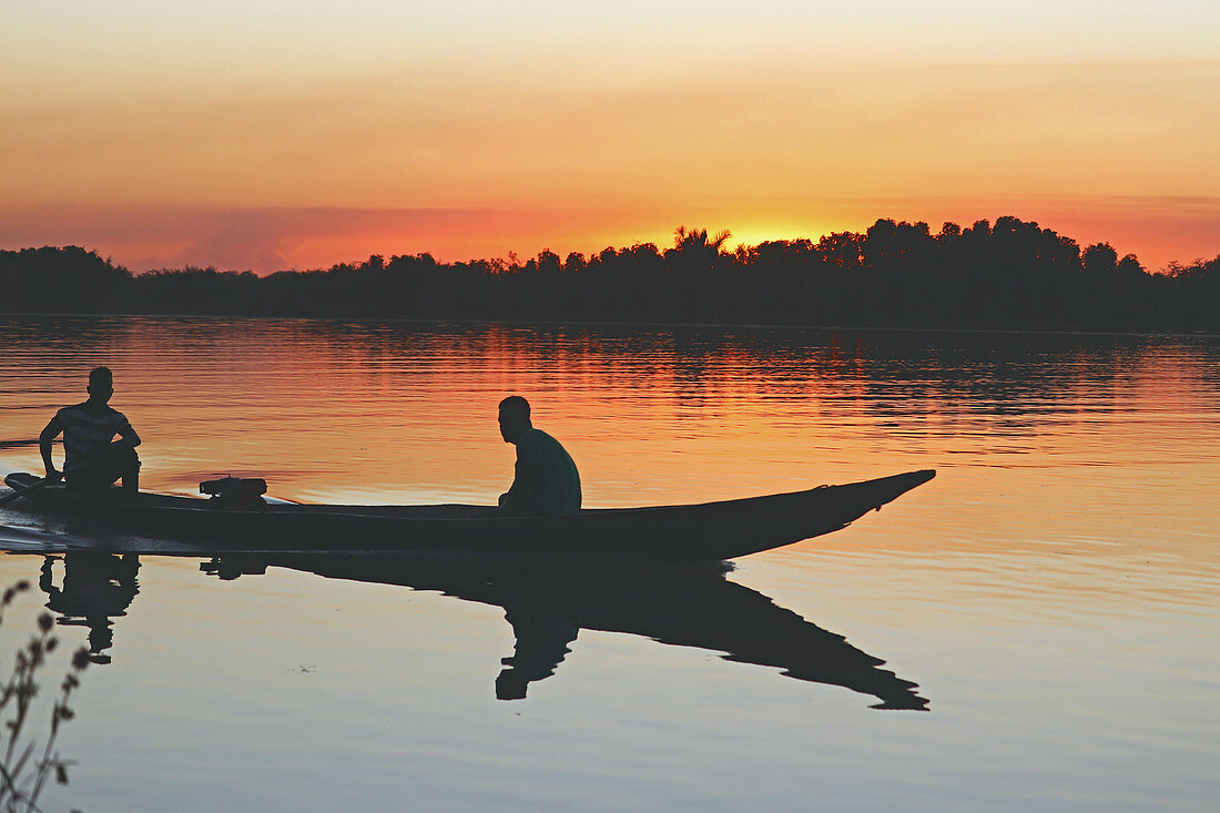 Gambia; Central River Region; Abendrot am Gambia-Fluss bei Kuntaur; zwei Männer sitzen in einem Boot in der Nähe des Ufers