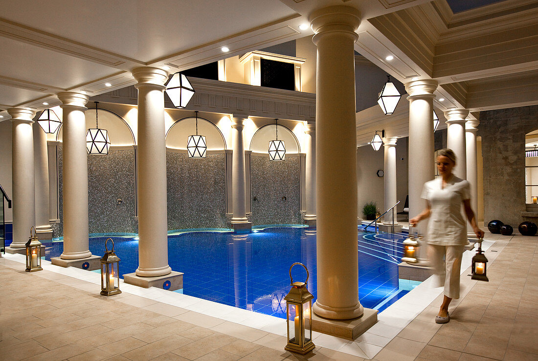 Evening shot of Spa therapist carrying lamps inside an intrioer pool room. Bath, United Kingdom