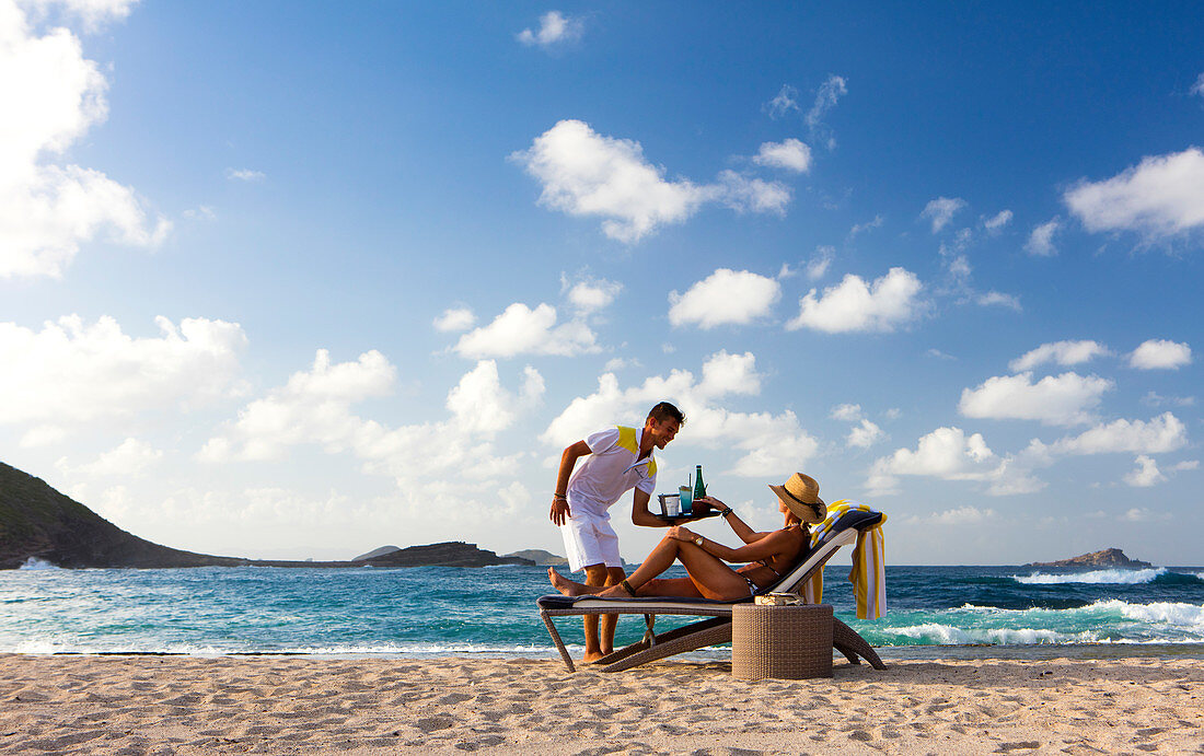 Strandservice. Frau, die vom Kellner am Strand bedient wird. St. Barths.