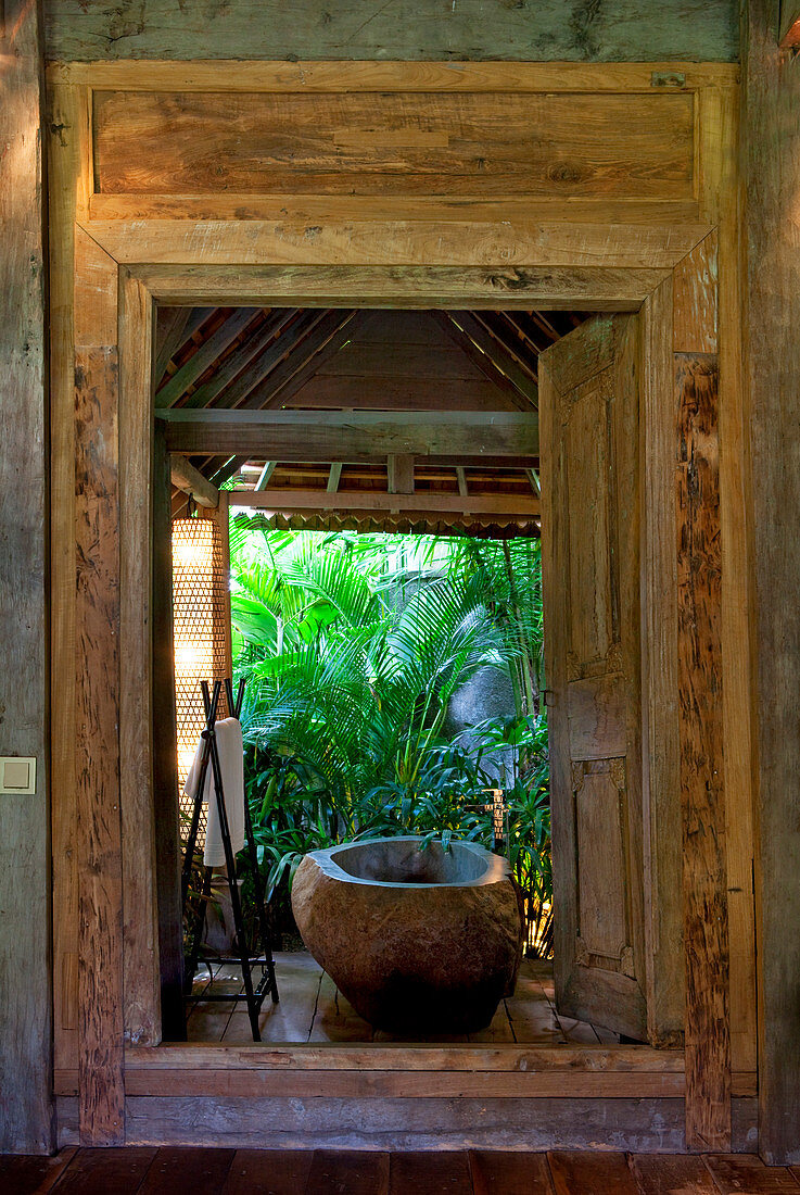 Stone bathtub set inside an open bathroom, in an old wooden house situated in the jungle. Bali, Indonesia.