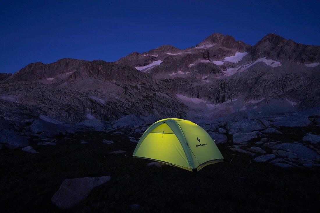 Von einem Scheinwerfer beleuchtetes Zelt mit den Gipfeln Bagüeñola oder Eriste im Hintergrund. Naturpark Posets-Maladeta. Aragon. Spanien.