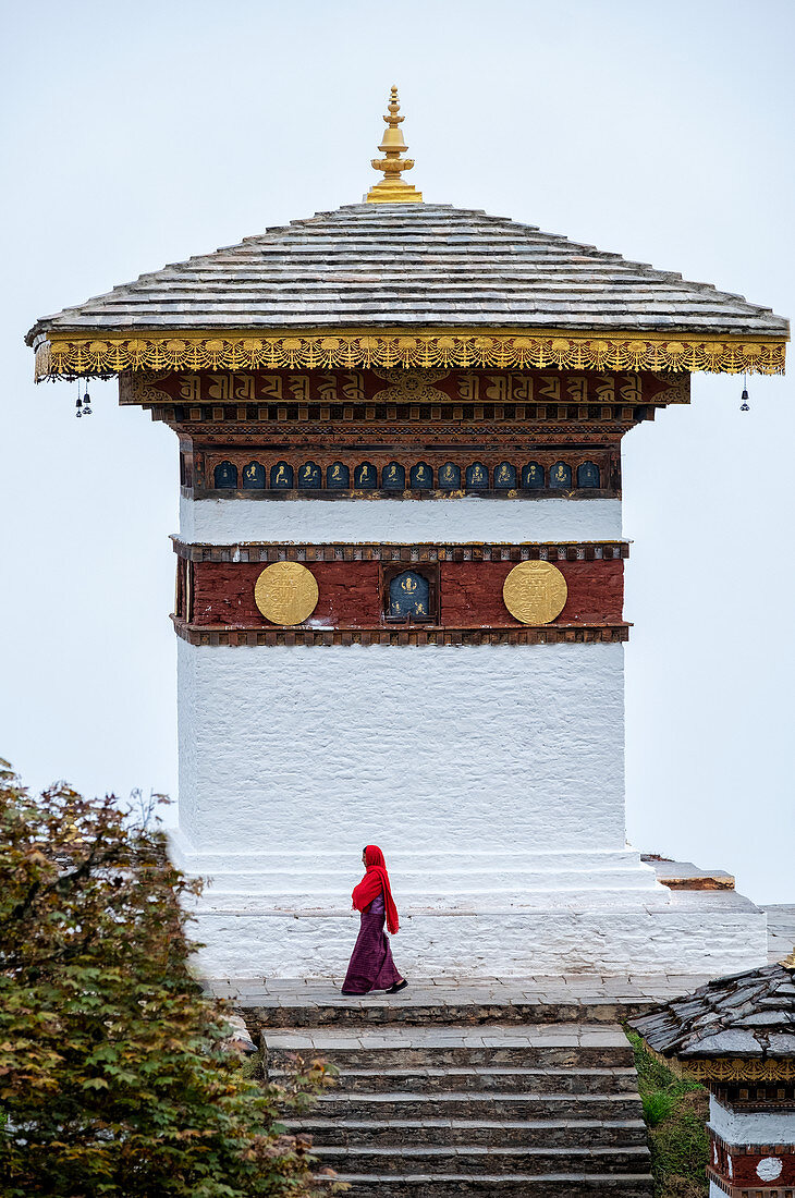 Einzelne Nonne, die an Tempel am Dochula-Pass, Bhutan, Asien vorbei geht