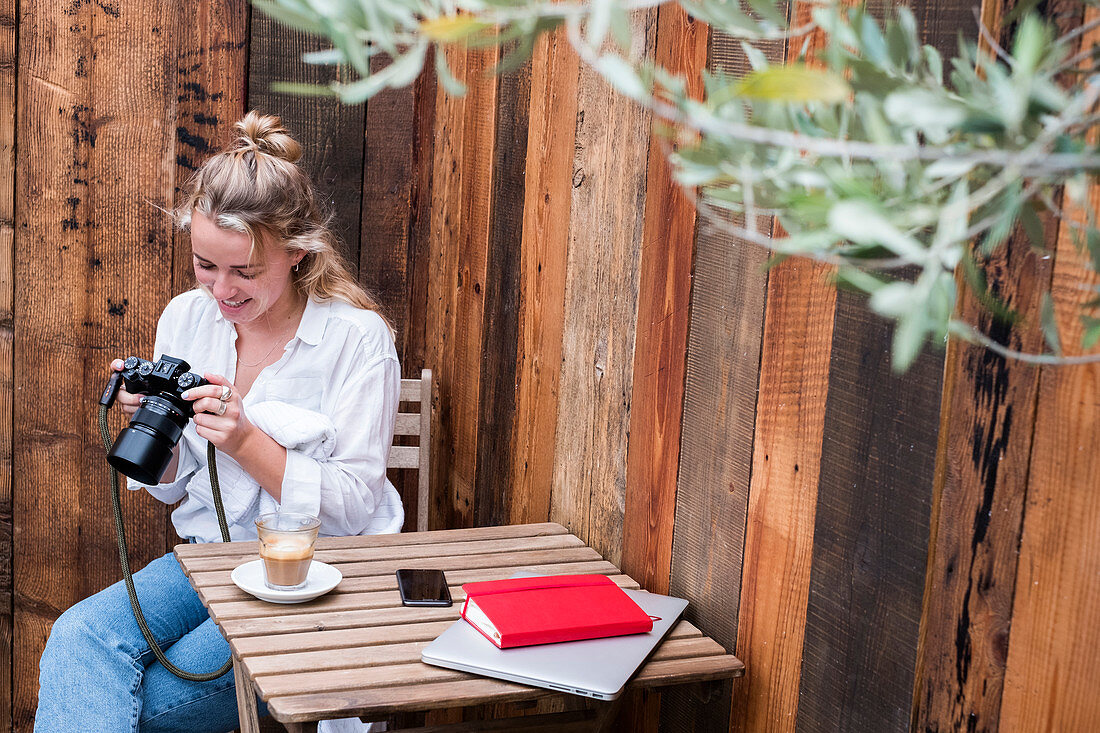 Young blond woman alone at an outdoor table, looking at digital camera display.