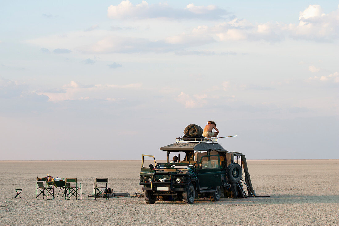 Ein Mann steht auf einem Geländewagen, der auf den Makadikadi-Salzpfannen in Botswana geparkt ist