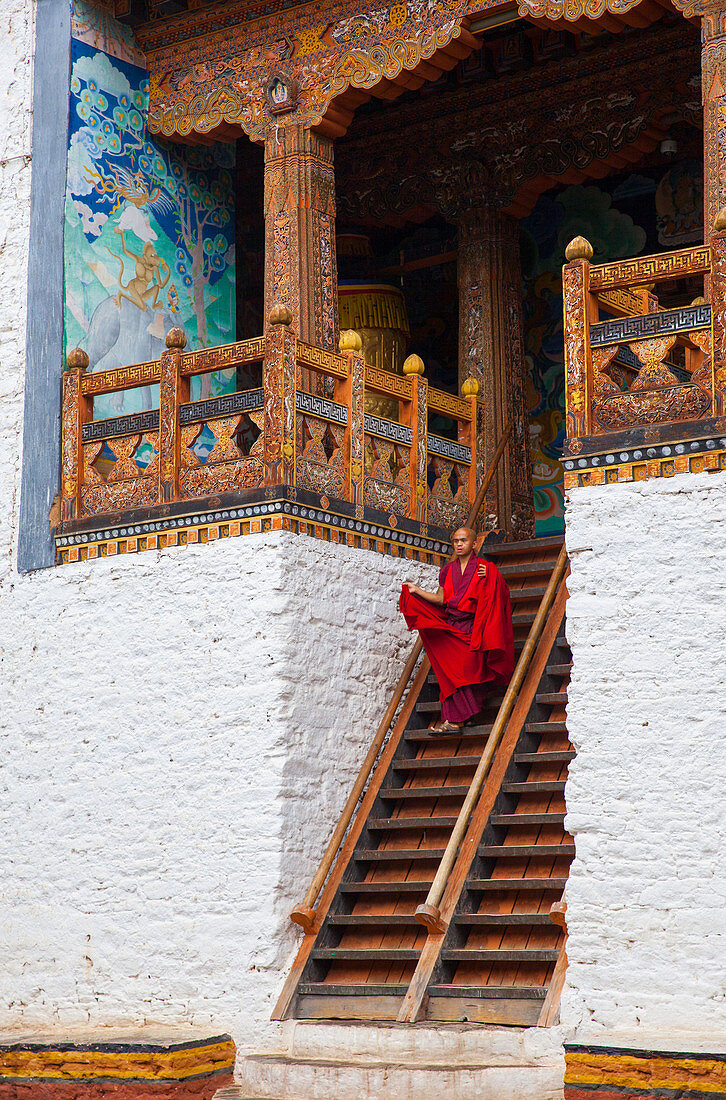 Ein buddhistischer Mönch in leuchtendem Rot, der eine Treppe in einem bhutanischen Tempel hinabsteigt. In Bhutan, Asien