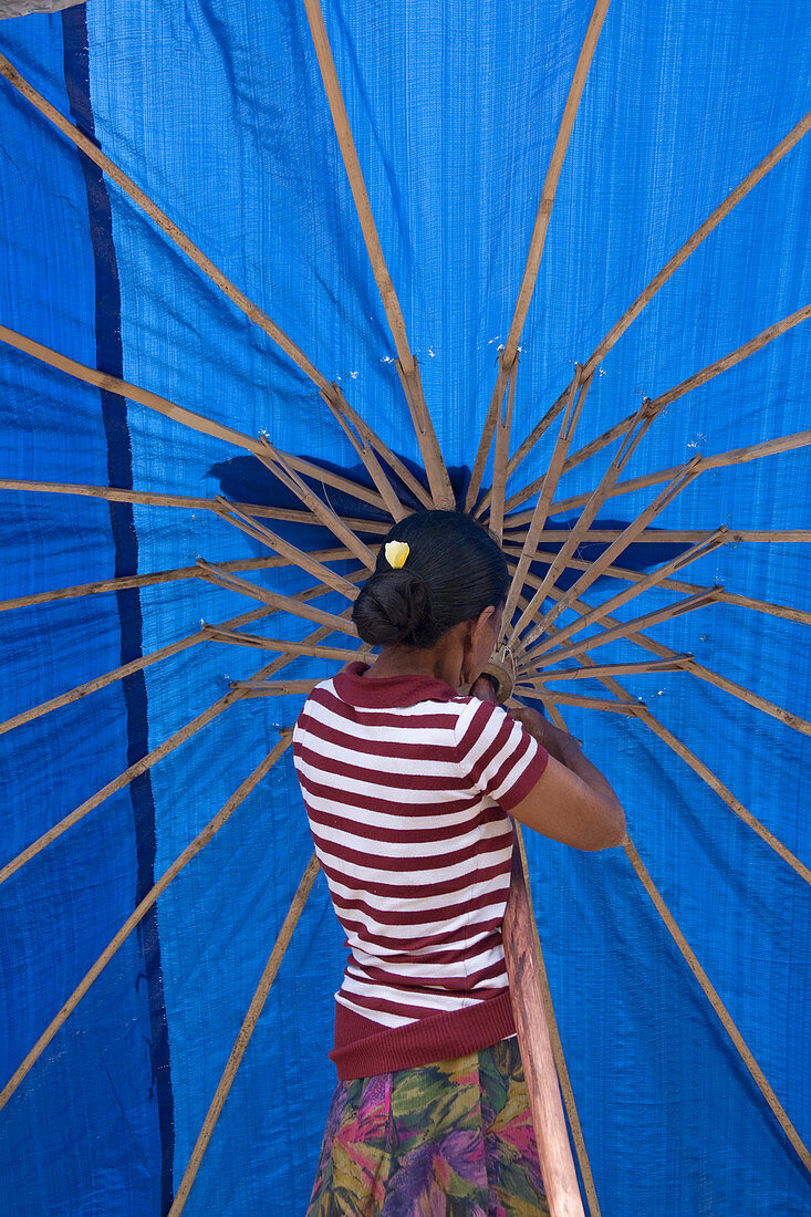 A balines woman in a striped blouse, opening a bright, blue umbrella in the market. Singaraja, Bali.