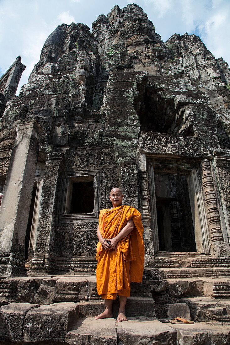 Buddhist monk stands proudly in front of the Bayon Temple in Angkor Thom, Angkor Wat, near Siem Reap, Siem Reap Province, Cambodia, Asia