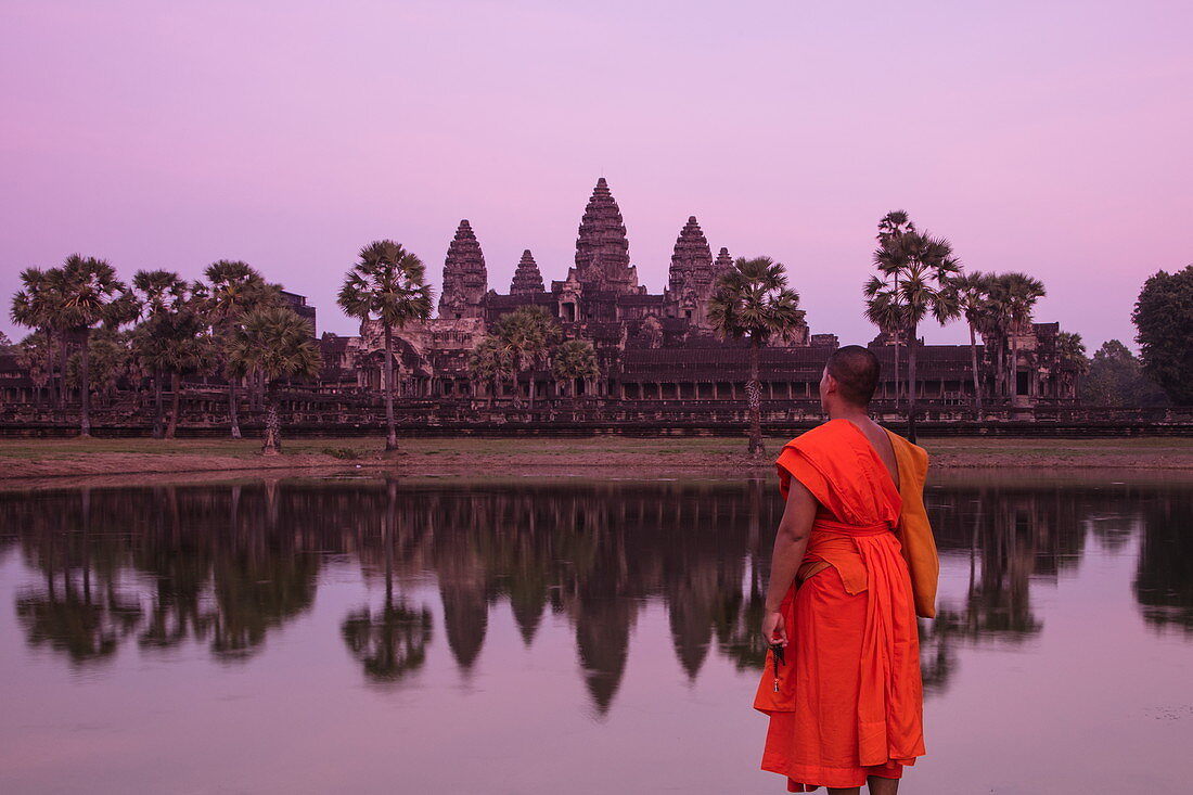 Buddhist monk stands by the moat and admires Angkor Wat temple at sunset, Angkor Wat, near Siem Reap, Siem Reap Province, Cambodia, Asia