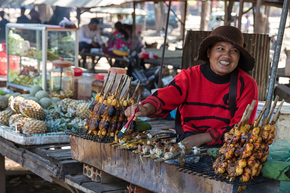 Happy woman with stuffed grilled frog at a street food stall in the market, Oudong (Udong), Kampong Speu, Cambodia, Asia