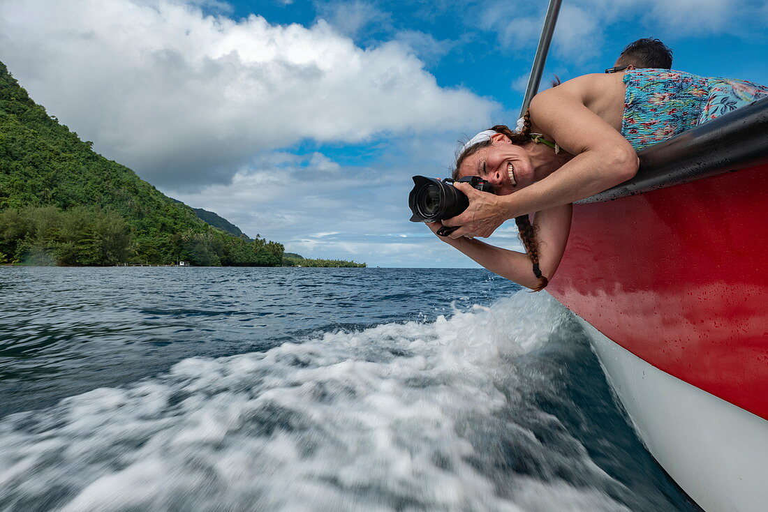 Lächelnde Frau mit Kamera beugt sich über Ausflugsboot um Wellen zu fotografieren, Tahiti Iti, Tahiti, Windward Islands, Französisch-Polynesien, Südpazifik