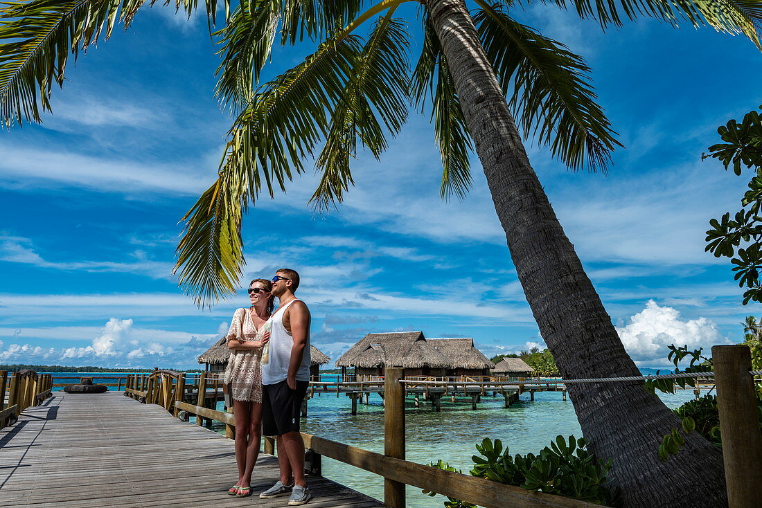 Junges Paar auf Holzsteg zu Überwasserbungalows im Sofitel Bora Bora Private Island Resort, Bora Bora, Leeward Islands, Französisch-Polynesien, Südpazifik